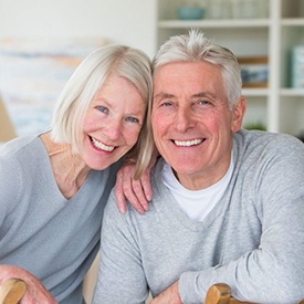 elderly couple wearing gray sweaters and smiling with dental implants in Acworth 